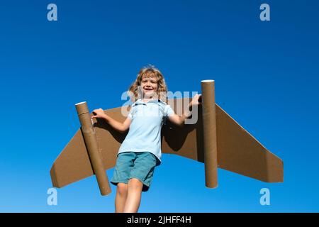 Kid with toy jetpack outdoor. Child playing on sky with cardboard wings. Spring travel and adventure. Stock Photo