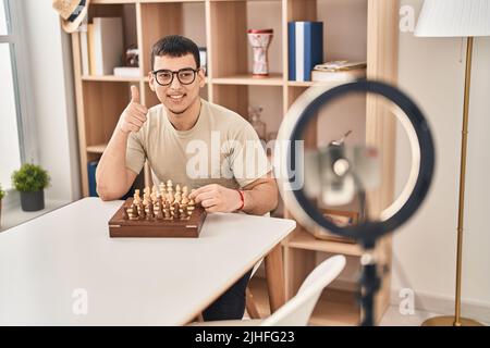Young arab man doing chess tutorial smiling happy and positive, thumb up doing excellent and approval sign Stock Photo