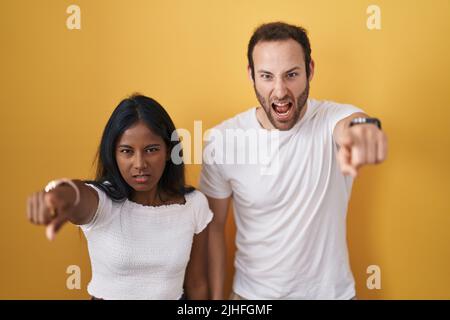 Interracial couple standing over yellow background pointing displeased and frustrated to the camera, angry and furious with you Stock Photo