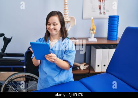 Down syndrome woman wearing physiotherapy uniform using touchpad at physiotherapist clinic Stock Photo