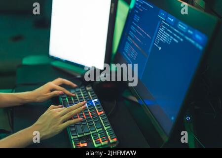 Unrecognizable young woman sitting in a gamer armchair typing on a backlit keyboard. Hacking concept. High quality photo Stock Photo