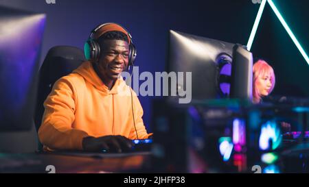 Focused african american male player wearing a beanie and a sweatshirt, sitting in a comfortable gaming armchair in front of a giant computer screen. High quality photo Stock Photo