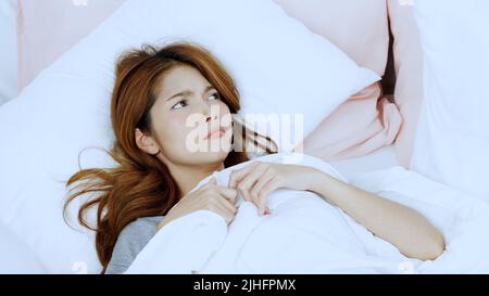 A closeup of a beautiful young woman looking puzzled lying in bed Stock Photo
