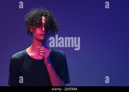 Relaxed stylish awesome curly man in black t-shirt posing isolated on color pink blue studio background. Cool fashion offer. Virtual Reality New Stock Photo