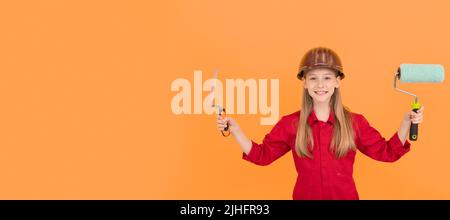 happy teen child in builder hard hat with paint roller and spatula on orange wall Stock Photo