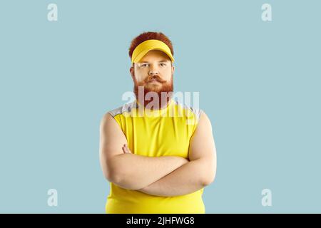 Angry displeased fat athlete standing with his arms crossed isolated on blue background Stock Photo