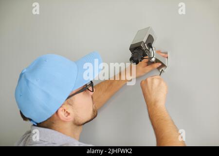Young male worker installing surveillance CCTV camera on wall inside the building Stock Photo