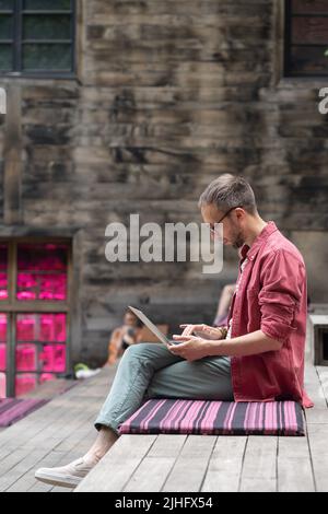 Focused man freelance web developer writing code while working on laptop at outdoor office Stock Photo