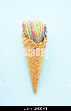 Colorful sour jelly candies in sugar sprinkles in an ice cream cone on a light blue background. Flat lay, copy space, vertical. Stock Photo