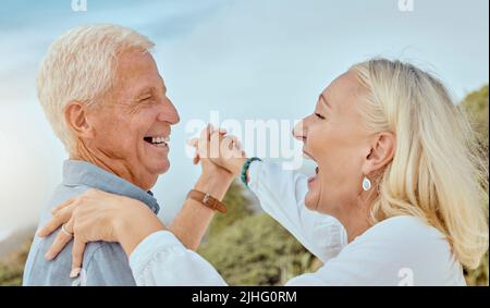 A happy mature caucasian couple enjoying fresh air on vacation at the beach. Smiling retired couple dancing outside Stock Photo