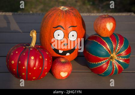 large orange pumpkin with a painted face, a painted decorative colored halloween pumpkins lie on a table in the garden as a decoration Stock Photo