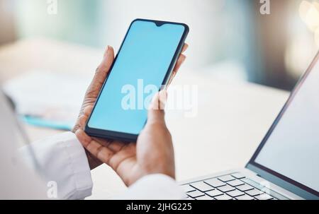 Above closeup african american woman doctor using her smart phone while working at a desk in her hospital office. Using wireless technology to Stock Photo
