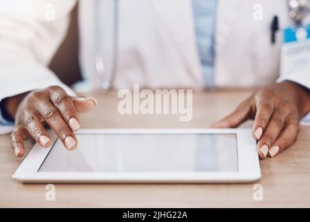Above closeup african american woman doctor using a digital tablet while working at a desk in her hospital office. Using wireless technology to Stock Photo