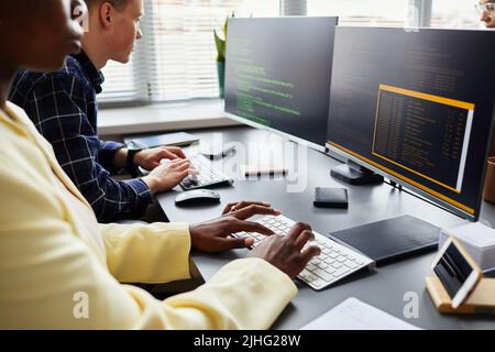 Close-up of colleagues sitting at table in front of monitors and typing on keyboard, they working with new software Stock Photo
