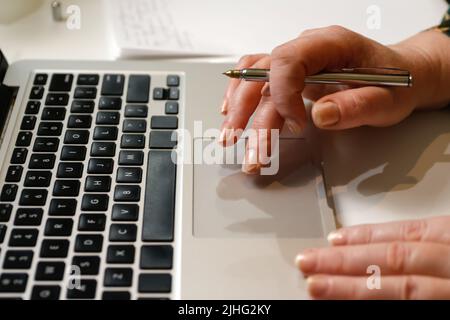 Defocus female hand holding pen. Unrecognizable elegant woman working on computer at office. Start or finish of a work day. Workspace. Paperwork. Time Stock Photo