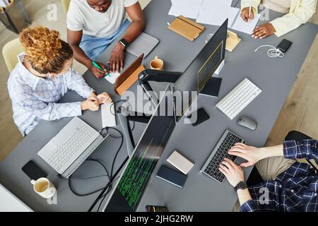 High angle view of group of programmers discussing development of new software sitting at table with computer monitors Stock Photo