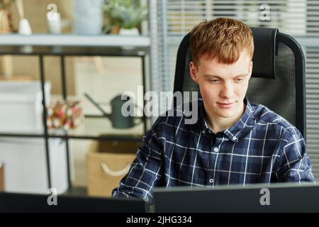Young IT specialist sitting in front of computer monitor and working with program at his workplace at office Stock Photo
