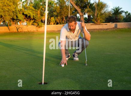 Pro golf player aiming shot with club on course. Male golfer on putting green about to take the shot. Stock Photo