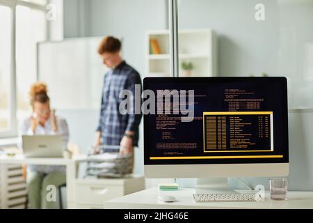 Close-up of computer codes of new software on monitor standing on office desk with programmers working in background Stock Photo