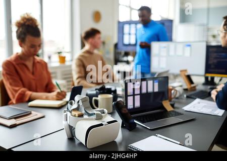 Horizontal image of VR glasses lying on table while programmers testing new software in background Stock Photo