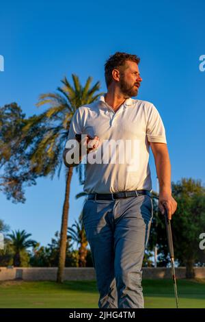 Portrait of young handsome golf player at golf club using smartphone. Stock Photo