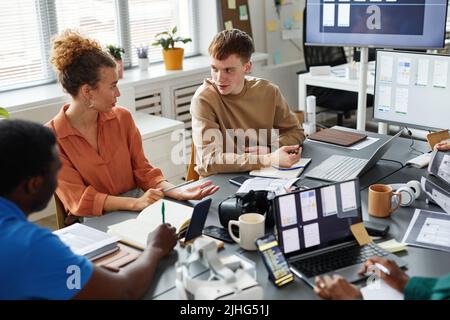 Team of programmers discussing and testing new software together at table during meeting at office Stock Photo