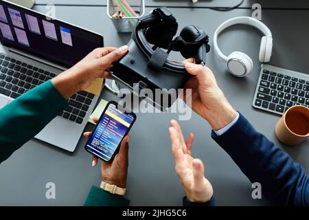 High angle view of developers connecting smartphone to virtual reality glasses to test new application during teamwork at table Stock Photo