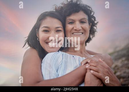 Portrait of a young hispanic woman spending the day at the beach with her elderly mother. Mixed race female and her mother smiling at the beach and Stock Photo