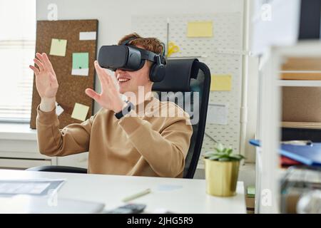 Young programmer sitting at table at office and gesturing, he testing virtual reality glasses Stock Photo