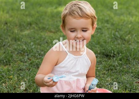Positive toddler kid playing with soap bubbles on grass in park Stock Photo
