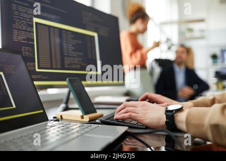 Close-up of young programmer typing codes to work with software while sitting at his workplace at office Stock Photo