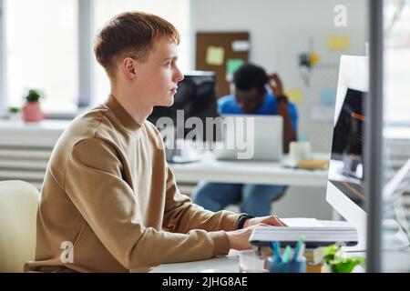 Profile view of young programmer working on computer in IT office typing data coding in software at his workplace Stock Photo