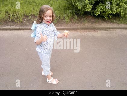 Funny blond blue eyed girl with ice cream stuck out tongue, shows Like gesture. Naughty playful. Stock Photo