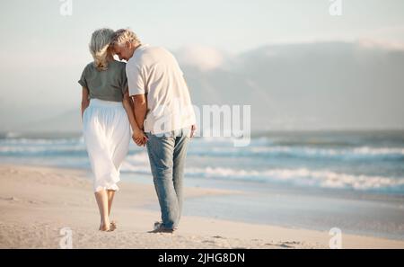 Back of a senior couple walking on a beach together. Senior couple holding hands and walking on the beach. Mature couple enjoying a vacation together Stock Photo