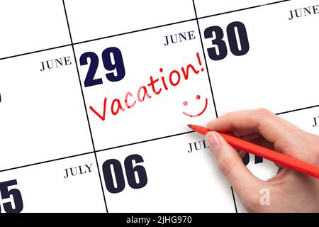 29th day of June. A hand writing a VACATION text and drawing a smiling face on a calendar date 29 June. Vacation planning concept. Summer month, day o Stock Photo