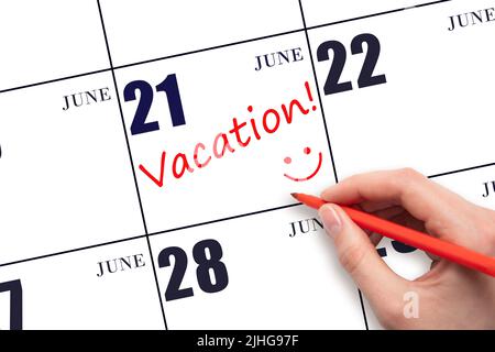 21st day of June. A hand writing a VACATION text and drawing a smiling face on a calendar date 21 June. Vacation planning concept. Summer month, day o Stock Photo