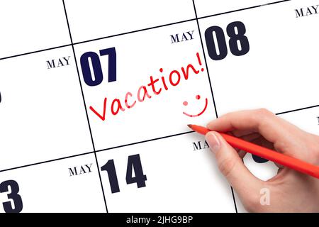 7th day of May. A hand writing a VACATION text and drawing a smiling face on a calendar date 7 May. Vacation planning concept. Spring month, day of th Stock Photo