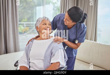 A hispanic senior woman in a wheelchair and her female nurse in the old age home. Mixed race young nurse and her patient in the lounge Stock Photo