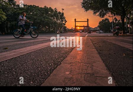 Guilin, China - August 2019 : Chinese Man riding on his bicycle behind zebra pedestrian crossing on Sanduo Lu street at dusk, Guangxi Province Stock Photo