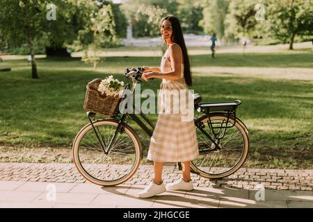 Pretty young woman with flowers in the basket of electric bike Stock Photo