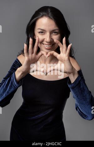 Young attractive smiling woman making heart shape gesture with hands. Smiling female Showing love symbol.  Heartfelt gratitude. Stock Photo