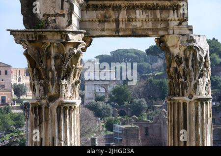 Looking towards the arch of Titus through the corinthian columns of the Temple of Vespasian and Titus in the Roman Forum, Central Rome, Lazio, Italy. Stock Photo