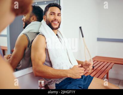 Fit athlete sitting on a bench talking to his friend. Two friends taking a break in the gym. Players bonding and talking before a match. Professional Stock Photo