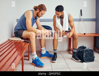 Two players bonding in their gym locker room. Two professional athletes using their cellphones together. Professional squash players talking and using Stock Photo