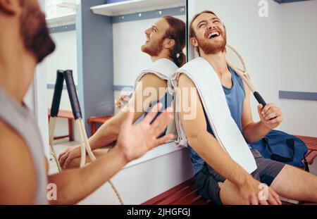 Cheerful squash players laughing and talking. Two friends taking a break from their match to relax. Happy friends bonding in the gym locker room. Two Stock Photo