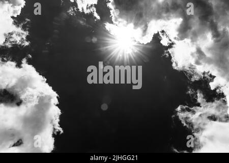 a heavenly landscape with a bright sun breaking through the clouds in a blue sky, black and white photo Stock Photo