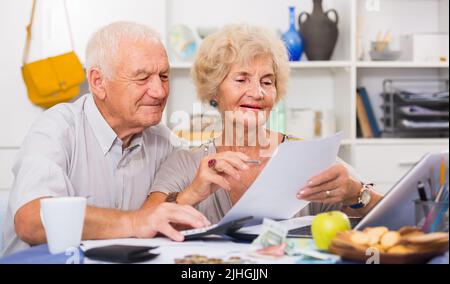 Happy senior spouses with bills and laptop Stock Photo