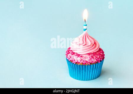 Celebration birthday cupcake with striped birthday candle and pink sprinkles on a blue background Stock Photo