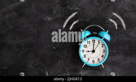 Twin bell alarm clock ringing against a chalkboard with copy space to side Stock Photo