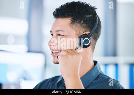 One happy hispanic call centre telemarketing agent talking on a headset while working in an office. Confident friendly male consultant operating a Stock Photo